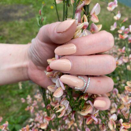 Schöne lange Nägel mit nude farbenden UV Gelfolien und Blumen in der Hand