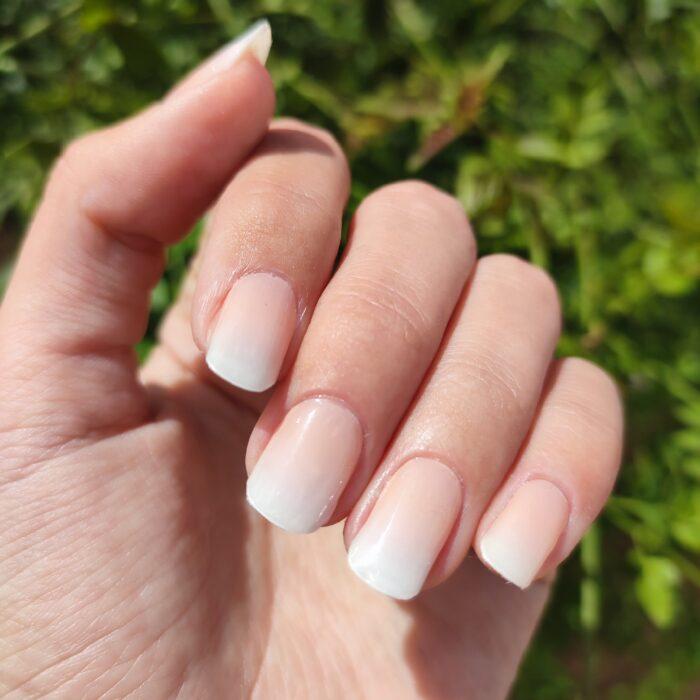 PEACH BABYBOOMER UV Gelnailz auf gepflegten Fingernägeln mit einer grünen Pflanze im Hintergrund