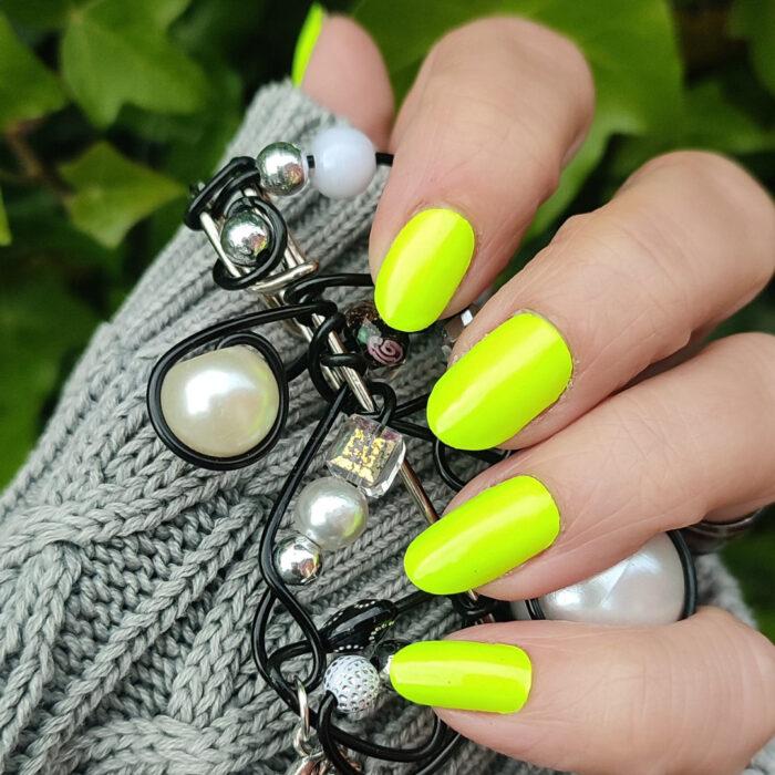 Tragefoto der GREEN neon Nailz im Sonnenlicht mit Brosche in der Hand