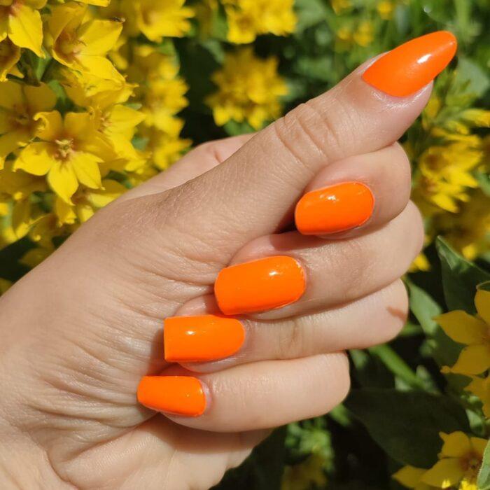 Stylische ORANGE neon Nailz im Sonnenlicht vor einem Blumenhintergrund