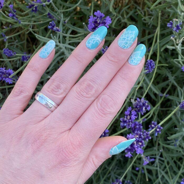 Türkise Nagelfolien mit Mandala-Muster, aufgeklebt und vor Blumen fotografiert.