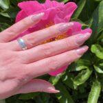 Nahaufnahme der LIGHT PINK glitter Nailz auf einer Hand, mit pinker Blume im Hintergrund.