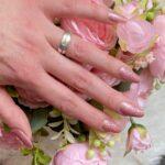 LIGHT PINK glitter Nailz auf einer gepflegten Hand, umgeben von einem floralen Hintergrund.