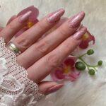 Eine Hand mit LIGHT PINK glitter Nailz, elegant präsentiert vor einem Hintergrund aus Blumen.