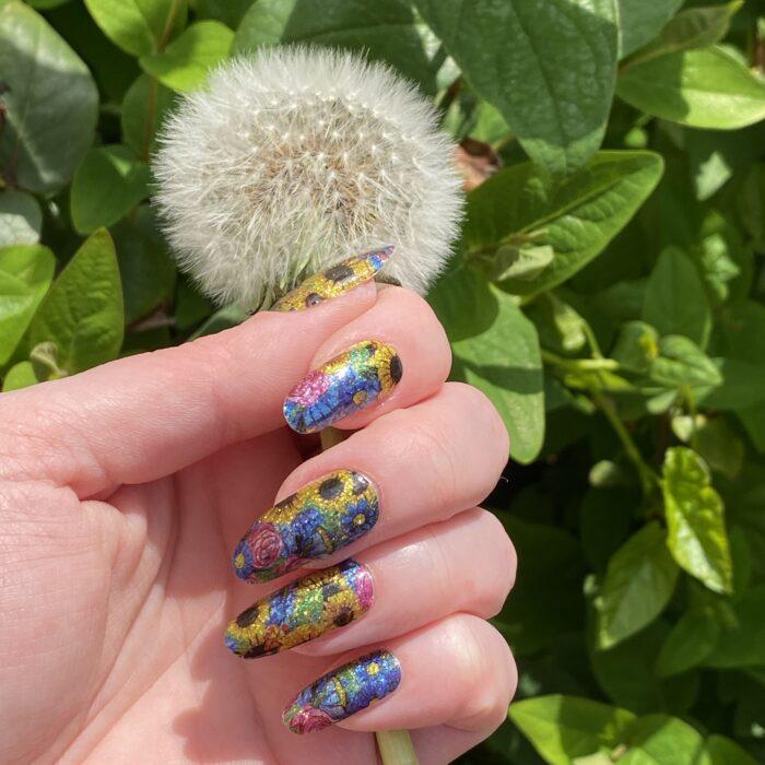 SUMMER BLOSSOM glitter Nailz aufgeklebt auf langen Nägeln einer Hand, die eine Pusteblume hält.