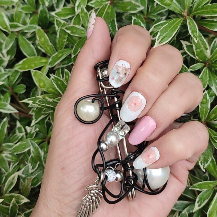 Hand mit SWEET SAFARI Nailz und Schmuck vor grünem Hintergrund