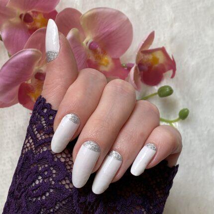 Nahaufnahme der aufgeklebten WHITE LUXE glitter Nailz mir einer rosafarbigen Blume im Hintergrund.